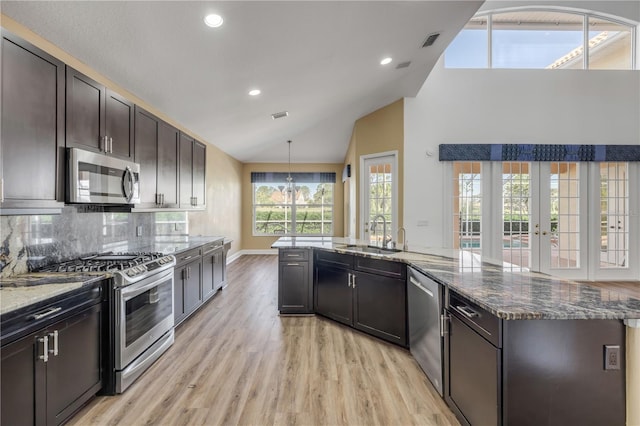 kitchen featuring light wood-style flooring, a sink, dark stone countertops, backsplash, and appliances with stainless steel finishes