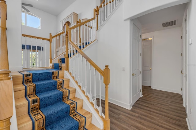 stairway with a high ceiling, plenty of natural light, wood finished floors, and visible vents