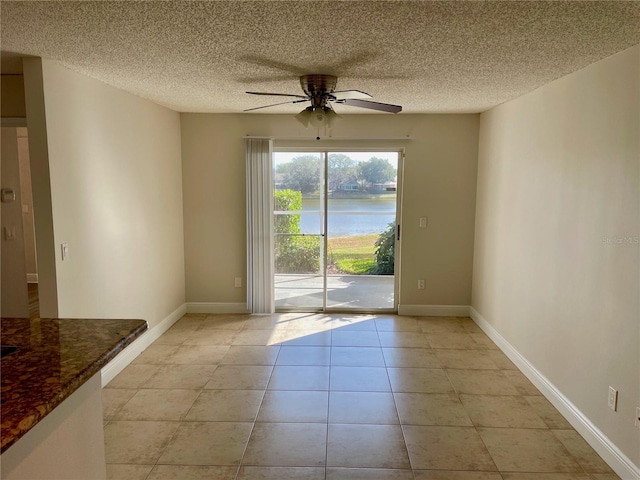 empty room with light tile patterned floors, baseboards, a ceiling fan, and a water view