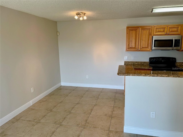 kitchen featuring brown cabinets, black range with electric stovetop, stainless steel microwave, dark stone counters, and baseboards