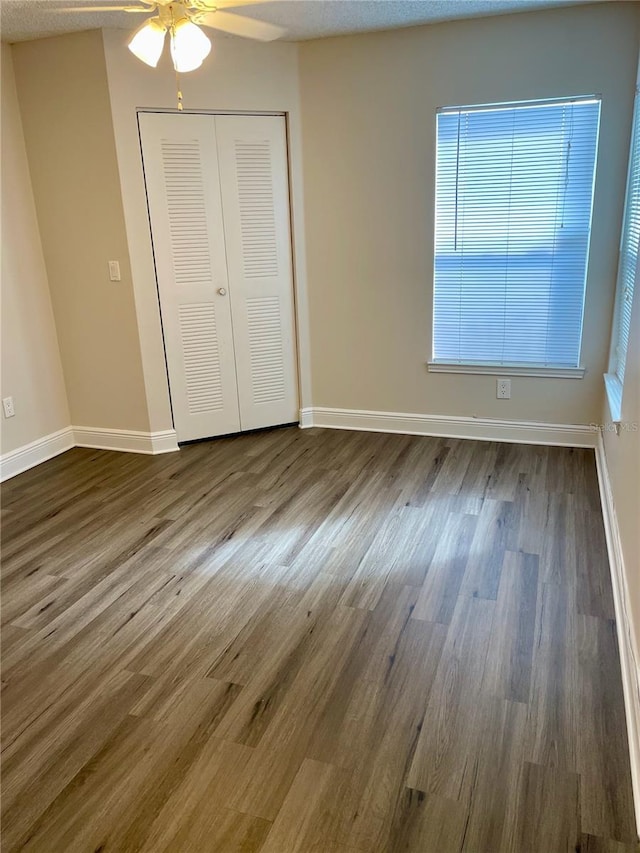 unfurnished bedroom featuring ceiling fan, a closet, baseboards, and dark wood-style floors