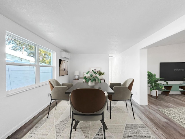 dining space featuring light wood-type flooring, baseboards, a textured ceiling, and a wall mounted AC