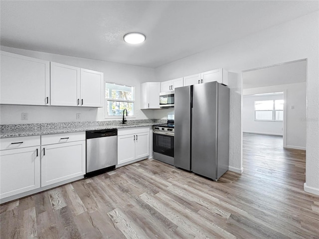 kitchen featuring white cabinetry, stainless steel appliances, light wood-style floors, and a sink