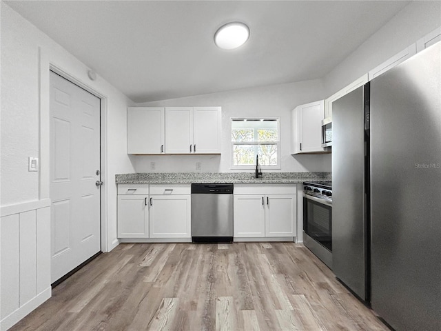 kitchen featuring light stone counters, light wood finished floors, a sink, stainless steel appliances, and white cabinets