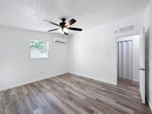 unfurnished room featuring visible vents, a wall unit AC, wood finished floors, a textured ceiling, and a ceiling fan