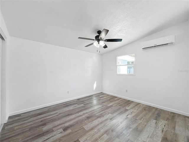 spare room with a textured ceiling, wood finished floors, a wall unit AC, baseboards, and ceiling fan