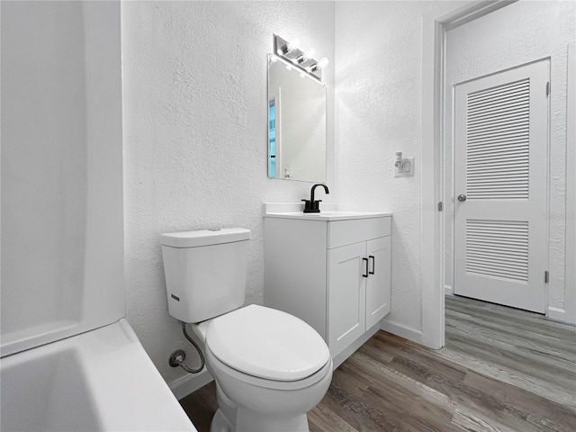 bathroom with toilet, wood finished floors, vanity, and a textured wall