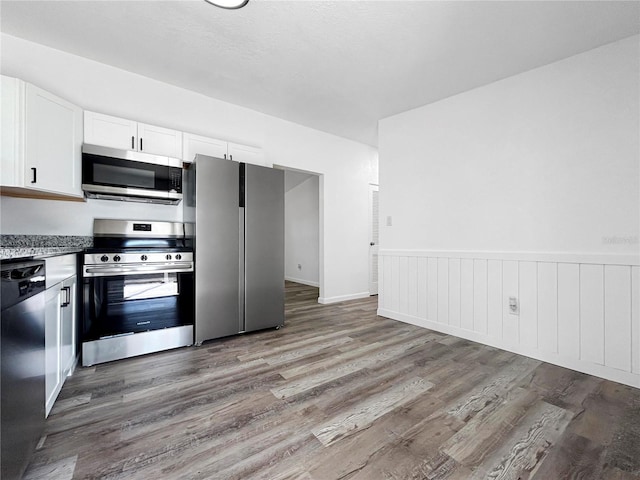 kitchen with a wainscoted wall, light wood-style flooring, white cabinets, and stainless steel appliances