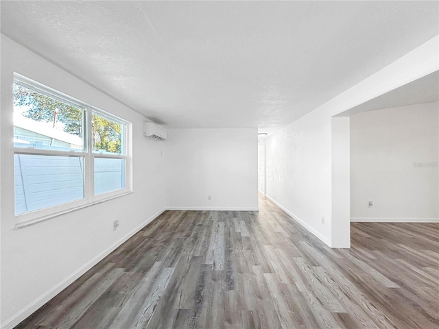 empty room featuring a textured ceiling, a wall mounted air conditioner, baseboards, and wood finished floors