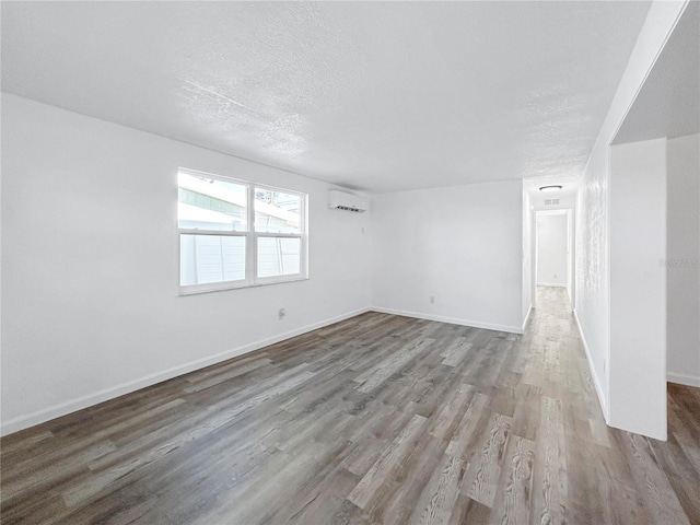 spare room featuring wood finished floors, baseboards, a wall mounted air conditioner, and a textured ceiling