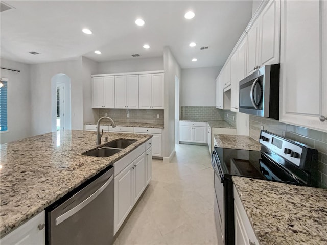 kitchen featuring a sink, light stone counters, arched walkways, and stainless steel appliances