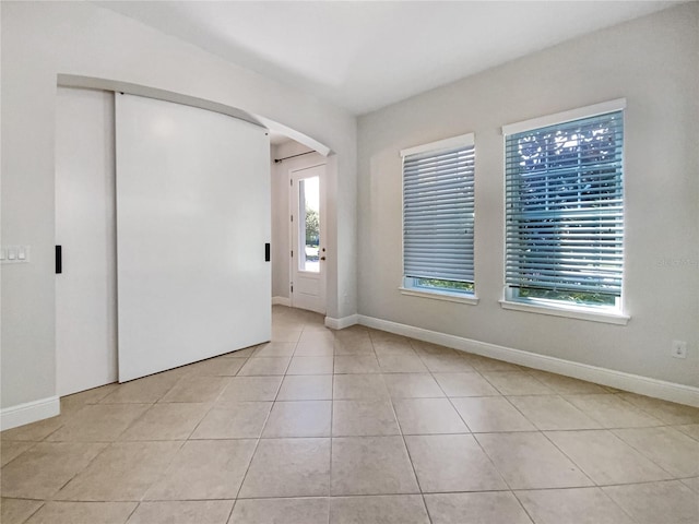 empty room featuring light tile patterned floors, baseboards, and arched walkways