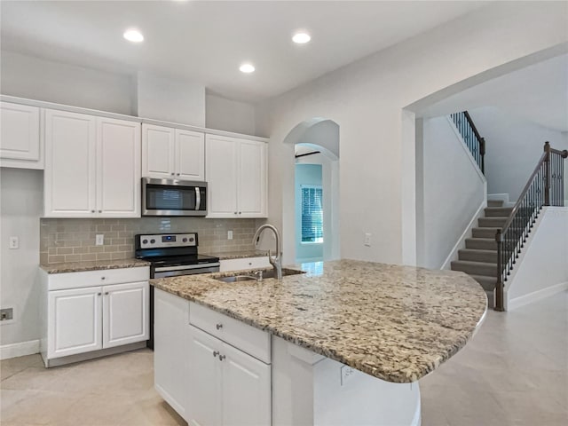 kitchen with a sink, stainless steel appliances, light stone counters, and white cabinets