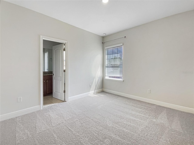 unfurnished bedroom featuring light colored carpet, connected bathroom, and baseboards