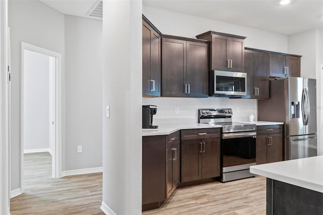 kitchen with light wood-type flooring, dark brown cabinetry, appliances with stainless steel finishes, light countertops, and decorative backsplash