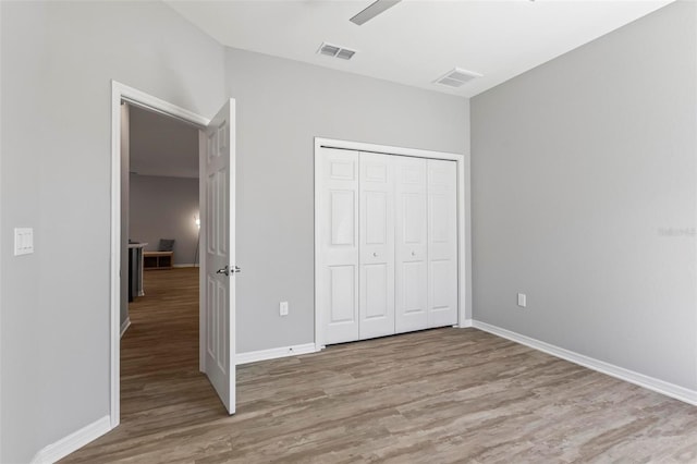 unfurnished bedroom featuring a closet, visible vents, baseboards, and wood finished floors