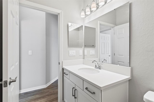 half bathroom with toilet, vanity, baseboards, and wood finished floors