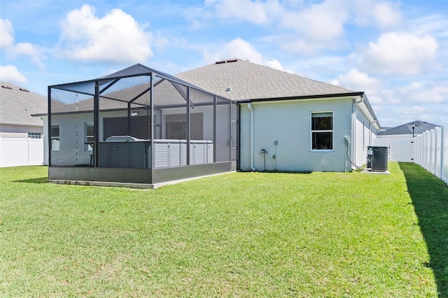 rear view of house with glass enclosure, a fenced backyard, a shingled roof, stucco siding, and a lawn