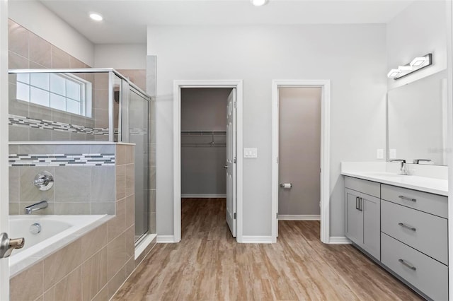 full bathroom featuring a spacious closet, wood finished floors, a stall shower, and tiled bath