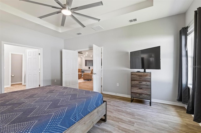 bedroom with light wood finished floors, visible vents, a raised ceiling, and baseboards