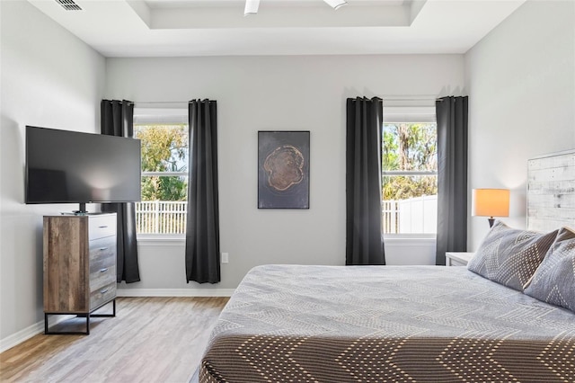 bedroom with multiple windows, a tray ceiling, and wood finished floors