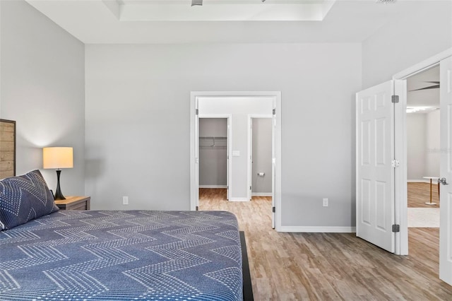 unfurnished bedroom with a raised ceiling, a spacious closet, wood finished floors, and baseboards