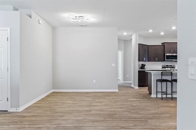 kitchen featuring light wood-type flooring, stainless steel appliances, light countertops, baseboards, and dark brown cabinets