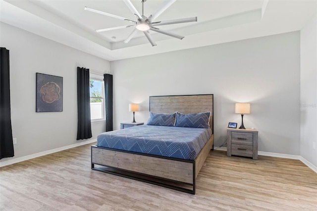 bedroom featuring ceiling fan, baseboards, light wood-type flooring, and a tray ceiling