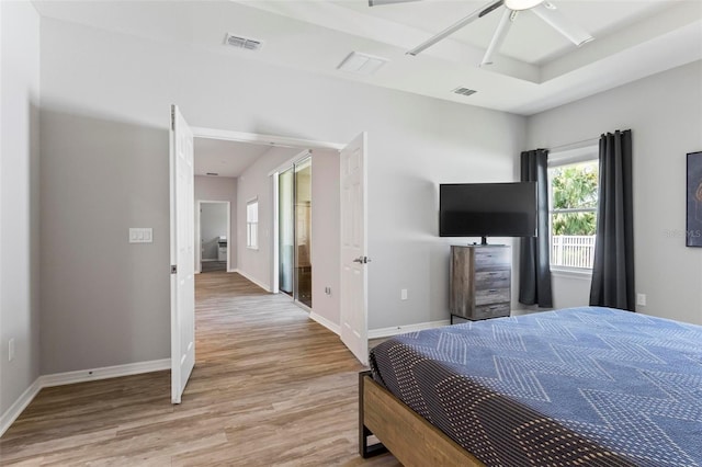 bedroom with a tray ceiling, wood finished floors, visible vents, and baseboards