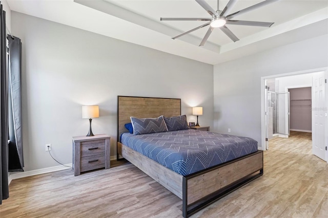 bedroom featuring a tray ceiling, baseboards, light wood-type flooring, and ceiling fan