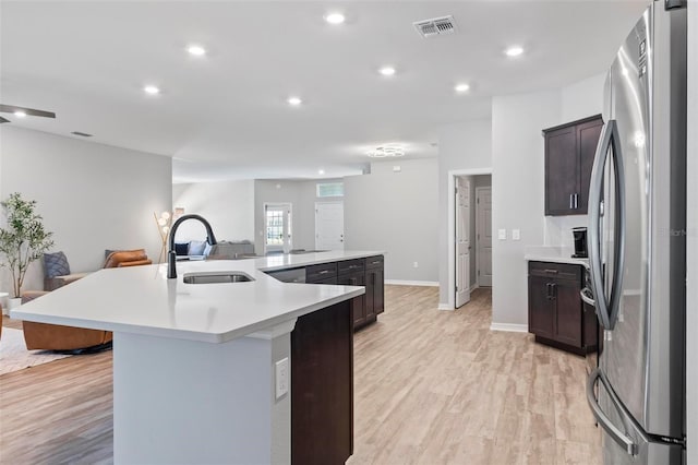 kitchen with visible vents, a sink, open floor plan, freestanding refrigerator, and a large island with sink