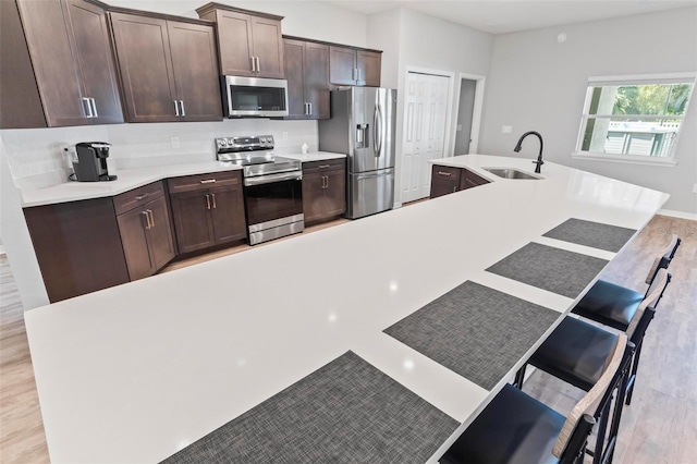 kitchen featuring a sink, dark brown cabinets, appliances with stainless steel finishes, a kitchen breakfast bar, and tasteful backsplash