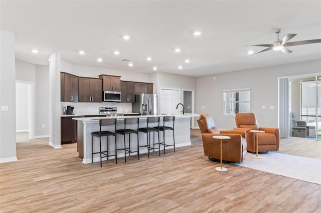 kitchen with dark brown cabinets, open floor plan, light countertops, appliances with stainless steel finishes, and a large island