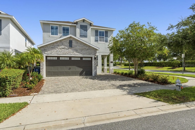 traditional-style home featuring stone siding, stucco siding, an attached garage, and decorative driveway