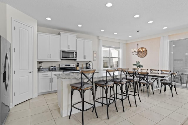 kitchen featuring a breakfast bar, an island with sink, light stone counters, appliances with stainless steel finishes, and white cabinets