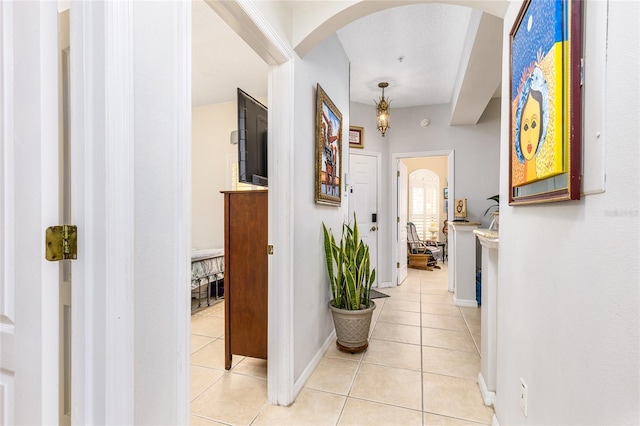 corridor with light tile patterned floors, arched walkways, and baseboards