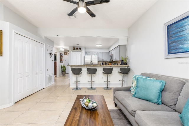 living room featuring visible vents, a ceiling fan, a textured ceiling, light tile patterned flooring, and baseboards