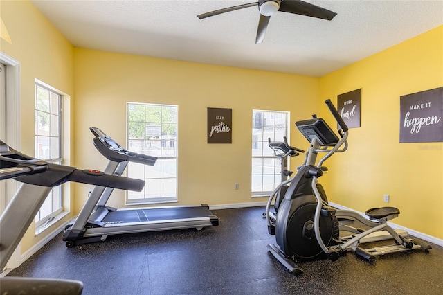 exercise area featuring baseboards, a textured ceiling, and a ceiling fan