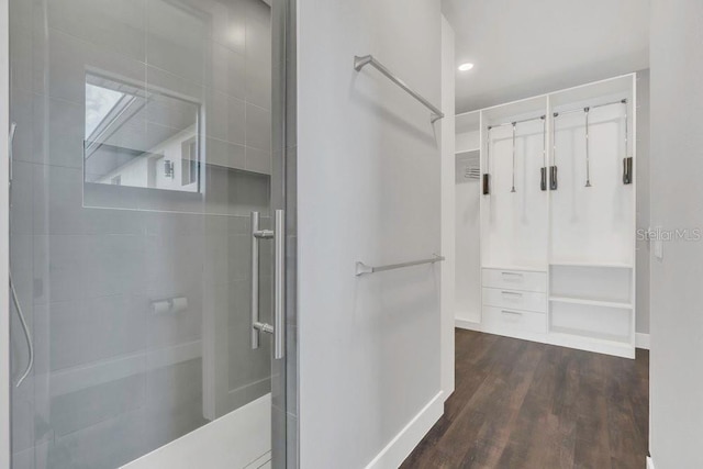 bathroom featuring a spacious closet, wood finished floors, baseboards, and tiled shower