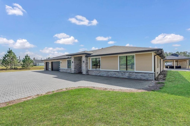 view of front facade featuring decorative driveway, stone siding, a front lawn, and an attached garage