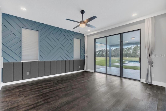 unfurnished room featuring baseboards, an accent wall, ceiling fan, and wood finished floors