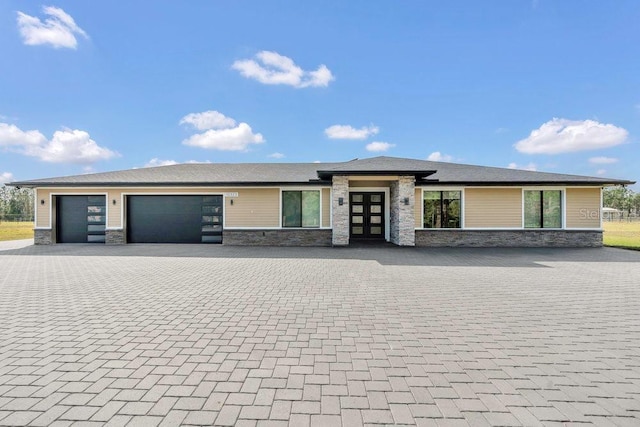 prairie-style house featuring decorative driveway, stone siding, and an attached garage