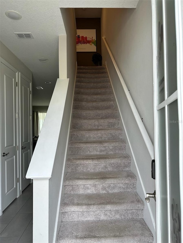 stairway featuring tile patterned flooring, visible vents, a textured ceiling, and baseboards