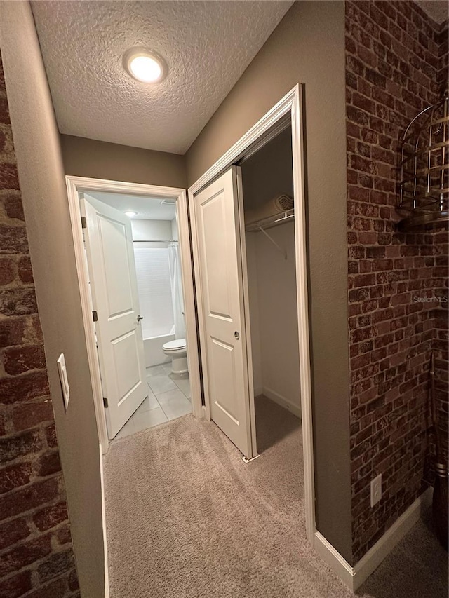 hallway with carpet, brick wall, and a textured ceiling