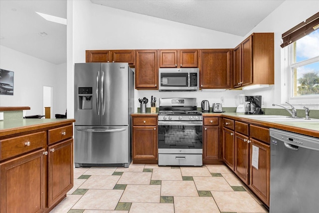 kitchen featuring lofted ceiling, a sink, light countertops, appliances with stainless steel finishes, and brown cabinets