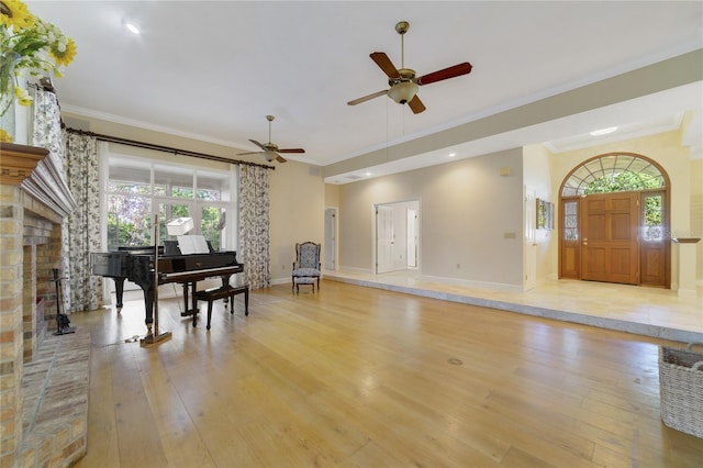 sitting room with a fireplace with raised hearth, light wood-style flooring, crown molding, and ceiling fan