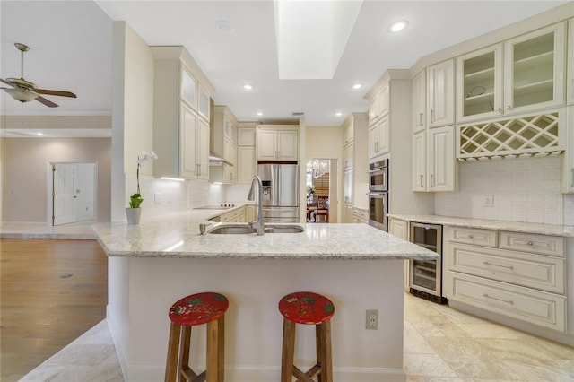 kitchen featuring cream cabinetry, a sink, stainless steel appliances, wine cooler, and a peninsula