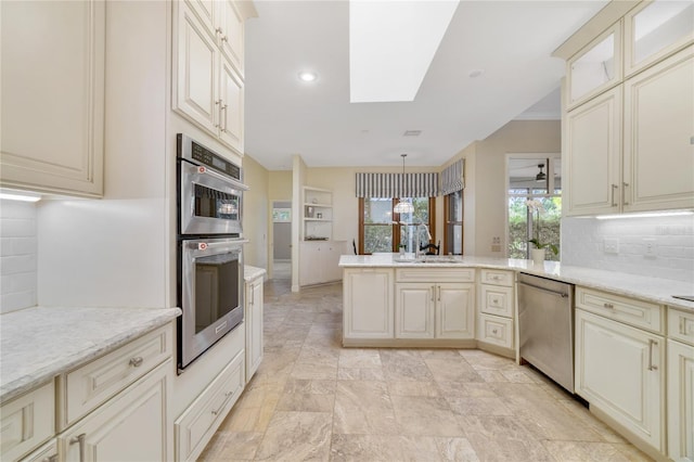 kitchen featuring a peninsula, a skylight, cream cabinetry, stainless steel appliances, and a sink