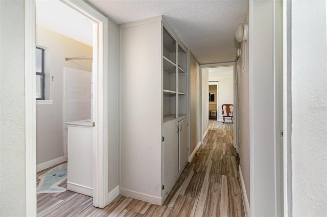 hallway with a textured ceiling, baseboards, and wood finish floors