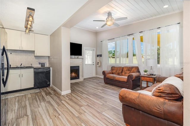 living room featuring baseboards, light wood-style floors, a warm lit fireplace, and ceiling fan